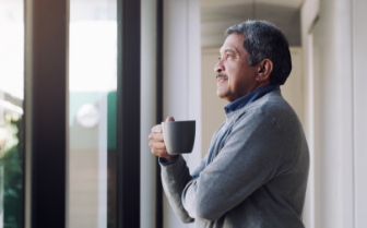 Man standing at window smiling and holding a cup of coffee.